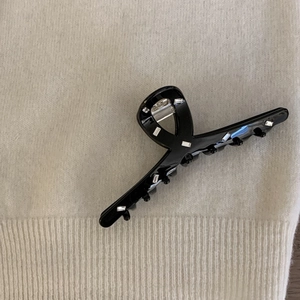 Close-up of black acetate hair claw clip with rectangle rhinestones on beige fabric