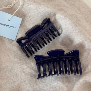 Detail view of two shiny sapphire blue hair claws on beige linen with a hanging tag