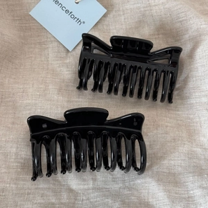 Detail of two glossy black resin hair claw clips on beige textured fabric background