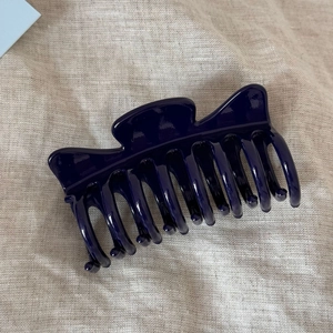 Close-up of a glossy navy blue resin hair claw clip on beige linen fabric background