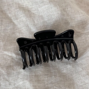 Detail view of the glossy black resin hair claw clip showing dual-teeth structure on linen