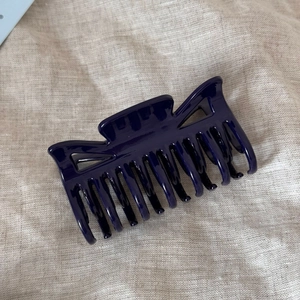 Detail of a deep purple glossy resin hair claw clip with multi-tooth design on fabric