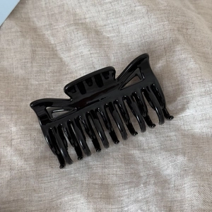 Close-up of a glossy black hair claw clip with geometric hollow design on linen cloth