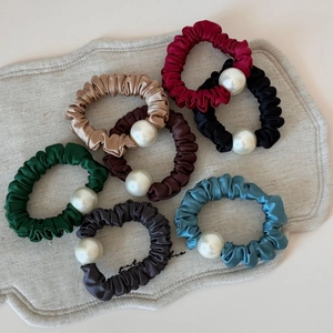 Elegant satin scrunchies set with pearls in seven assorted colors on a linen background