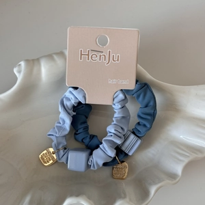Détail de chouchous bleus élastiques avec perle carrée et pendentif doré sur carte