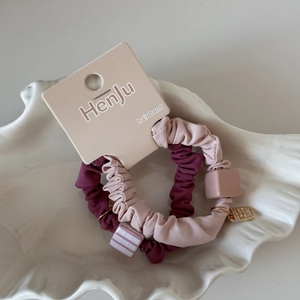 Détail de chouchous en tissu rose et bordeaux avec breloques cubes dans un plateau blanc
