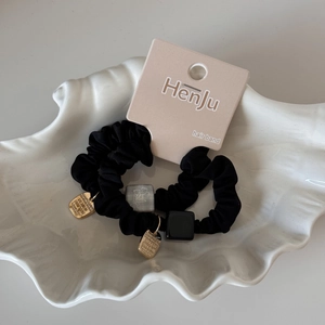 Détail de chouchous noirs avec étiquettes dorées et perles fleuries sur un plateau blanc