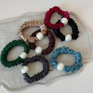 Detail of seven satin scrunchies with large pearls on grey linen display background
