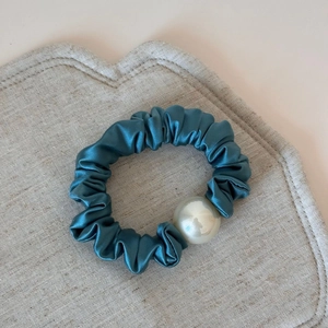Close-up of peacock blue satin hair scrunchie with elegant large pearl on linen texture