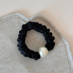 Close-up of black pleated satin scrunchie with a large pearl bead on a textured background