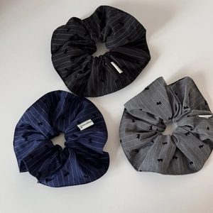 Detail of three striped scrunchies in black, blue, and grey with bow prints and fabric labels