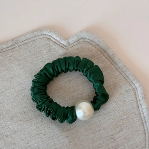 Detailed close-up of dark green satin scrunchie with a large white pearl bead ornament