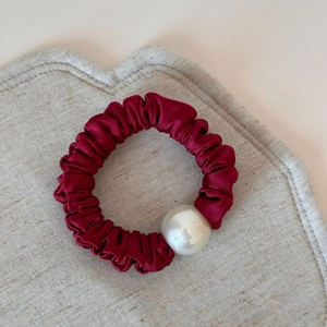 Detail of silk-like burgundy satin scrunchie featuring a white pearl accessory detail