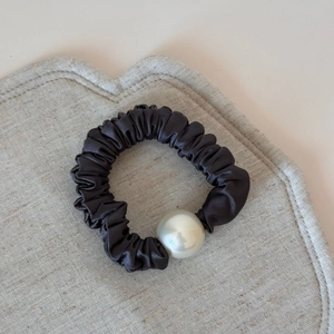 Macro detail of black satin scrunchie with a large white pearl bead on textured fabric
