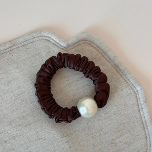 Detail view of a dark brown satin scrunchie with large pearl and elegant pleated texture