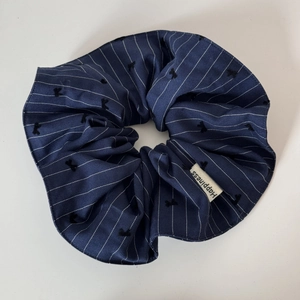 Detail of navy blue striped scrunchie featuring a bow design and Happiness fabric label