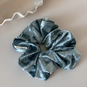 Detail view of mist blue velvet scrunchie featuring dark polka dots and brand label