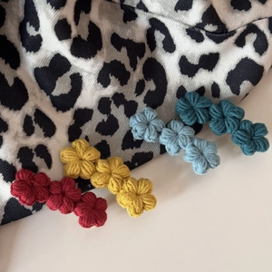 Detail of four colorful crochet flower hair clips in red, yellow, blue, and green colors