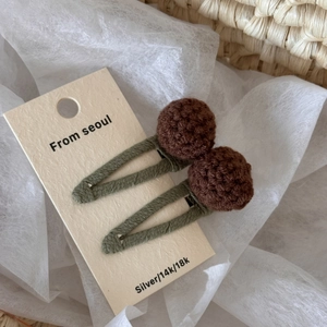 Detail of two handmade knit hair clips with green woven band and brown wool pom-poms