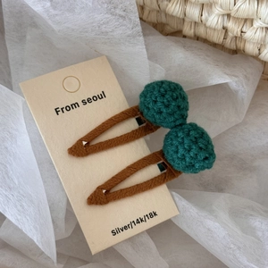 Detailed close-up of handmade crochet hair clips with green yarn balls on display card