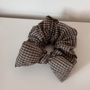 Close-up of brown plaid scrunchie with bow tie detail on a clean white background