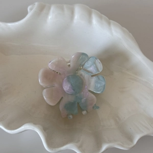 Détail d'une pince à cheveux fleurie en acétate avec texture marbrée pastel dans un plat