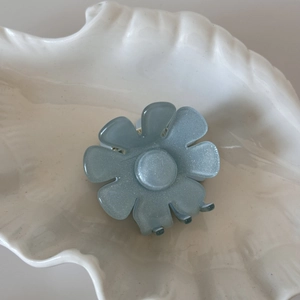 Détail d'une pince à cheveux fleur bleue avec paillettes sur un plateau blanc