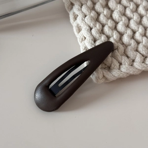 Détail de la texture cuir marron foncé et du clip en métal noir sur un tissu en maille