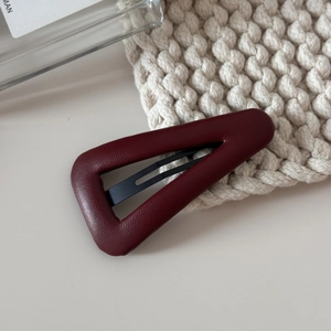 Vue détaillée de la pince à cheveux en cuir rouge foncé sur un fond tricoté blanc doux