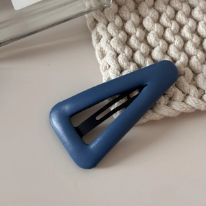 Détail de la pince à cheveux triangle en cuir bleu avec texture grainée et clip métal