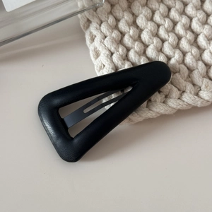Détail d'une pince à cheveux triangulaire en cuir noir avec texture sur tissu tricoté