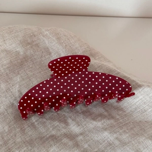 Detail of a burgundy hair claw clip with white polka dots on textured beige fabric