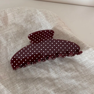 Close-up of retro burgundy hair claw clip with white polka dots on rustic linen texture