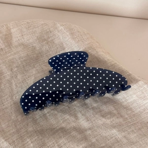 Detailed view of the wavy fan-shaped navy blue hair claw with white polka dots on linen fabric