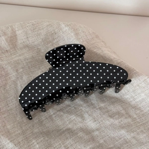 Close-up of black acetate hair claw clip with white polka dots on linen fabric
