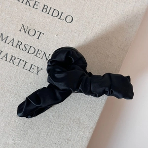 Detail einer großen Haarklammer mit elegantem, schwarzem, gefaltetem Satingewebe
