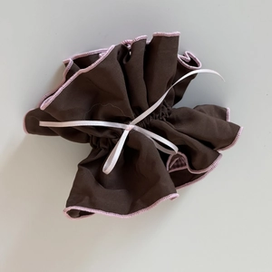 Detail of a brown pleated fabric scrunchie with pink edges and a white silk ribbon bow