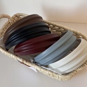 Five assorted colors of wide pleated PU leather headbands in a beige woven basket