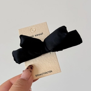 Close-up of black padded bow hair clip held by hand on m seoul brand card