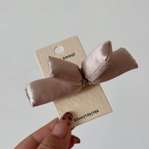 Detail of champagne satin bow hair clip on premium white textured display card