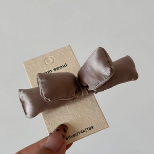 Detailed view of a champagne brown satin bow hair clip on a branded cream display card