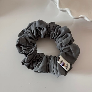 Gros plan sur un chouchou gris plissé avec une étiquette Happy et texture douce