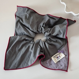 Détail d'un chouchou gris avec motif fleuri, nœud en ruban violet et étiquette de marque
