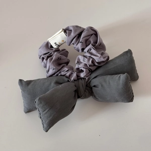 Détail macro du chouchou floral gris-violet avec grand nœud foncé et étiquette en tissu