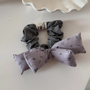Détail d'un chouchou en tissu gris avec nœud violet et motifs floraux élégants