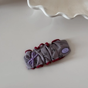 Détail d'un chouchou en tissu gris à fleurs avec nœud violet et étiquette faite main