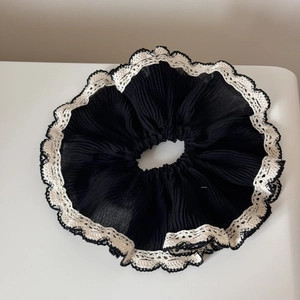 Close-up of black oversized scrunchie featuring delicate beige lace edges and wavy trim