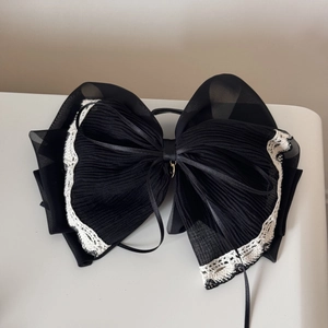 Detailed close-up of large black layered organza bow with white lace edges and gold charm