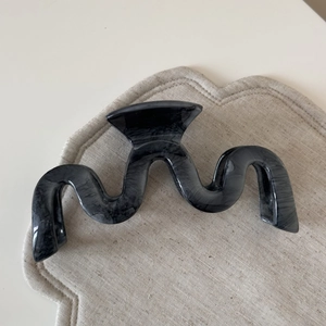 Macro detail of wave shaped marble pattern hair claw clip on soft textured background