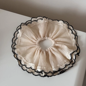 Close-up of beige ruffled scrunchie with delicate black and white lace crochet edging